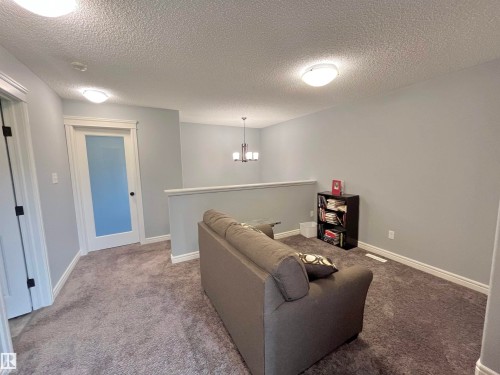 Carpeted upper-level landing featuring a half-wall railing, a frosted glass panel door, and ceiling-mounted flush lighting - 108 South Creek Wynd, Stony Plain, AB 