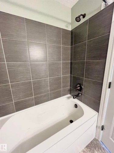 White bathtub with dark gray rectangular wall tiling, featuring matte black fixtures and a matching shower head - 108 South Creek Wynd, Stony Plain, AB 