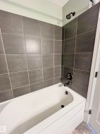 White bathtub with dark gray rectangular wall tiling, featuring matte black fixtures and a matching shower head - 