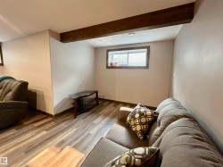 Finished lower level space featuring exposed wood-finish beam, recessed lighting, and wood-finish flooring - 