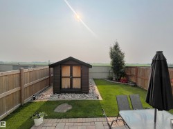 Expansive backyard featuring a lush lawn, a storage shed on a gravel bed, and a paved patio area - 