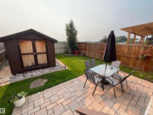 Backyard featuring an expansive paver patio, mature wood fencing, a dedicated storage shed, and a lush lawn - 108 South Creek Wynd, Stony Plain, AB 