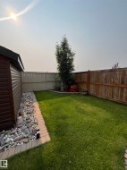 Expansive backyard featuring a manicured lawn, a built-in storage shed, a decorative rock border, a mature tree, and privacy fencing - 