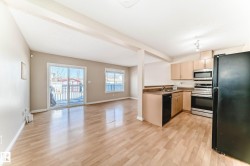 Open-concept living area featuring wood-finish flooring, a kitchen with light wood cabinetry, stainless steel appliances, and a black refrigerator, a sliding glass door leading to a back deck, and a window providing natural light - 
