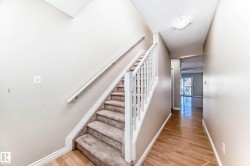 Carpeted staircase with white balusters and handrail, neutral wall paint, and wood-finish flooring extending into a hallway with a flush-mount ceiling light - 