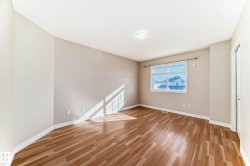 Spacious room featuring wood-finish flooring, neutral-toned walls, a single window with horizontal blinds, and a flush-mount ceiling light - 