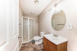 Bathroom featuring a corner shower enclosure, a wood-finish vanity with an integrated sink, an oval wall mirror, and patterned floor tiles - 
