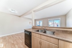 Kitchen with light wood-finish cabinetry, a double basin stainless steel sink, and a black built-in dishwasher - 