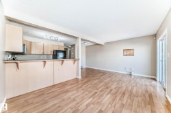 Open-concept living space featuring wood-finish flooring, a kitchen pass-through with breakfast bar, track lighting, and sliding patio doors - 