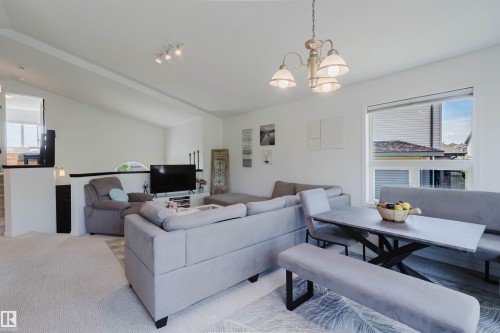 Open-concept living area featuring vaulted ceilings, a window with horizontal blinds, carpet flooring, a dining area with a chandelier, and a partial wall separating spaces - 1743 Melrose Crescent Sw, Edmonton, AB 