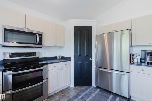 Kitchen featuring stainless steel appliances, light-toned cabinetry, dark countertops, and tile flooring - 1743 Melrose Crescent Sw, Edmonton, AB 