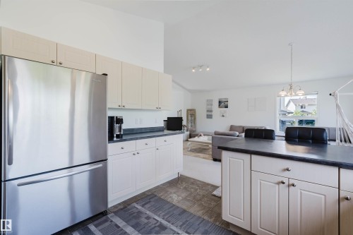 Kitchen featuring stainless steel refrigerator, light-toned cabinetry, dark countertops, and tile flooring - 1743 Melrose Crescent Sw, Edmonton, AB 