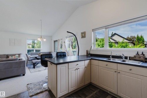Kitchen featuring light-toned cabinetry with dark countertops, a double basin sink, and a large window - 1743 Melrose Crescent Sw, Edmonton, AB 