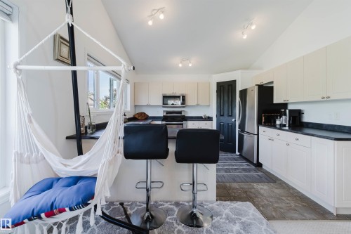 Kitchen featuring white cabinetry, dark countertops, stainless steel appliances, and a vaulted ceiling with track lighting - 1743 Melrose Crescent Sw, Edmonton, AB 