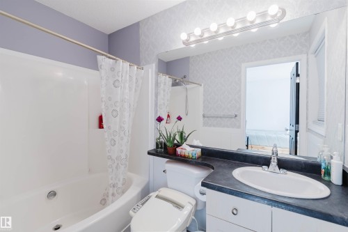 Bathroom featuring a white bathtub, vanity with an integrated sink, wall-mounted lighting, and patterned wallpaper accents - 1743 Melrose Crescent Sw, Edmonton, AB 