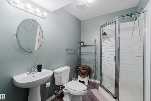 Bathroom featuring a pedestal sink, oval mirror, wall-mounted light fixture, and a corner shower enclosure with frosted glass panels - 1743 Melrose Crescent Sw, Edmonton, AB 