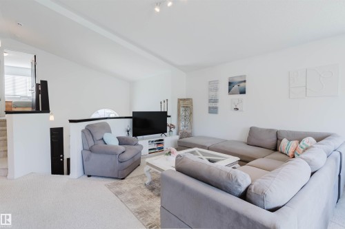 Vaulted ceiling living space featuring light-toned carpeting, a built-in partial wall with a dark cap, and a semicircular arch window - 1743 Melrose Crescent Sw, Edmonton, AB 