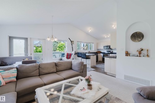 Vaulted ceilings enhance the main living area, featuring a decorative wall niche, a built-in kitchen island with a breakfast bar, and stainless steel appliances - 1743 Melrose Crescent Sw, Edmonton, AB 
