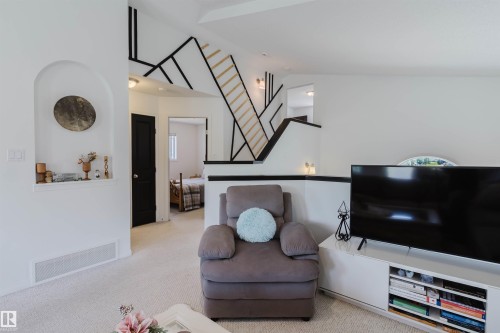 Carpeted living space featuring a built-in niche, dark interior doors, and a partial staircase with geometric accents - 1743 Melrose Crescent Sw, Edmonton, AB 