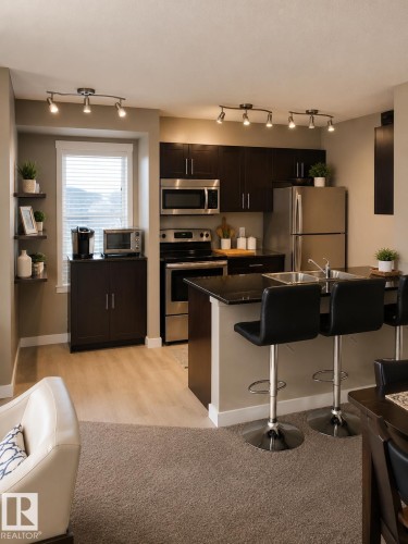 Kitchen area featuring dark wood-finish cabinetry, stainless steel appliances, track lighting, and a breakfast bar with dual basin sink - 128 1510 Watt Drive Sw, Edmonton, AB 