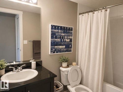 Bathroom featuring a dark vanity with an integrated sink, polished chrome faucet, and a wall-mounted mirror - 128 1510 Watt Drive Sw, Edmonton, AB 