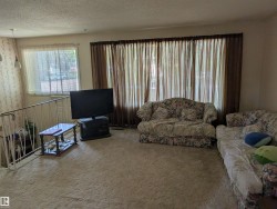 Living area featuring a large window with sheer and blackout curtains, carpeted flooring, and a white metal railing - 