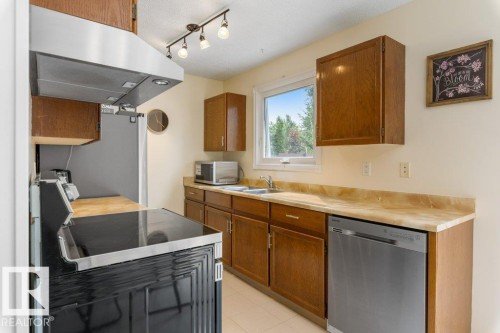 Kitchen featuring wood cabinetry, light-toned countertops, a stainless steel dishwasher, and a window above the sink - 18609 54 Avenue, Edmonton, AB 