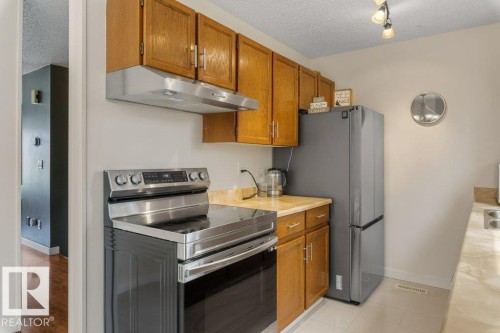 Kitchen featuring wood-finish cabinetry, stainless steel range hood, stainless steel electric range, and light-toned countertops - 18609 54 Avenue, Edmonton, AB 