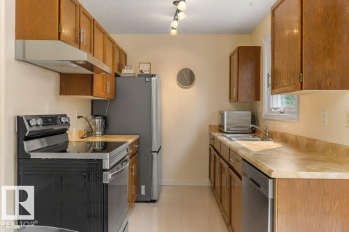 Galley-style kitchen featuring wood cabinetry, stainless steel appliances, light-toned countertops, and recessed lighting - 18609 54 Avenue, Edmonton, AB 