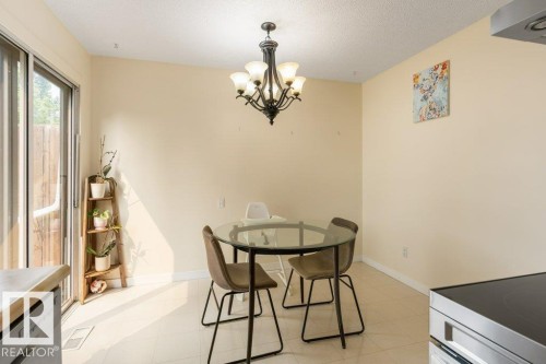 Dining area featuring a glass-top table, tile flooring, and a multi-bulb chandelier - 18609 54 Avenue, Edmonton, AB 