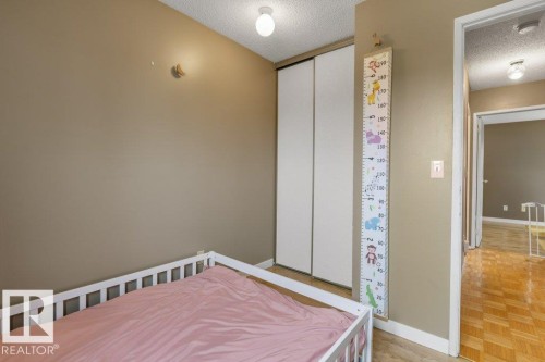 Bedroom featuring neutral wall color, textured ceiling, flush-mount lighting, and white sliding closet doors - 18609 54 Avenue, Edmonton, AB 