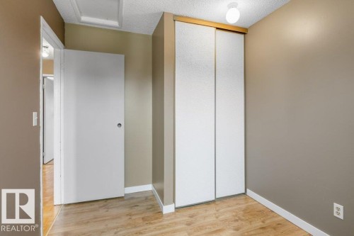 Interior room featuring wood-finish flooring, light tan wall paint, white trim, and a built-in closet with sliding doors - 18609 54 Avenue, Edmonton, AB 