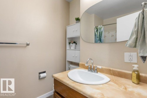 Bathroom vanity with an integrated basin, wood-finish cabinetry, and a stone-finish countertop - 18609 54 Avenue, Edmonton, AB 