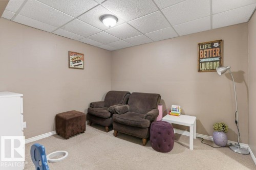 Interior space featuring light-colored carpet, neutral wall paint, and a white grid-patterned ceiling with a flush-mount light fixture - 18609 54 Avenue, Edmonton, AB 