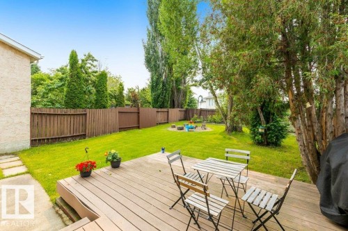 Expansive backyard featuring a wood-finish deck, lush green lawn, mature trees, and a privacy fence - 18609 54 Avenue, Edmonton, AB 