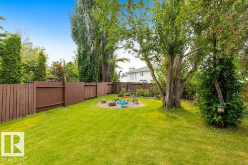 Expansive backyard featuring a green lawn, mature trees, and a perimeter brown wood fence - 18609 54 Avenue, Edmonton, AB 
