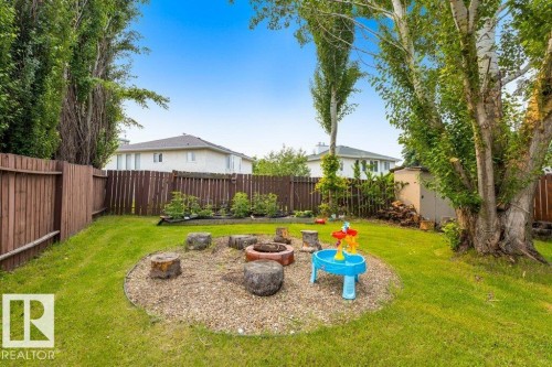 Expansive private backyard featuring a gravel-based fire pit area with tree stump seating, mature trees, a storage shed, and a privacy fence - 18609 54 Avenue, Edmonton, AB 