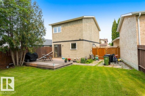 Expansive backyard featuring a large lawn, a spacious wooden deck with direct access from the interior, and mature perimeter trees providing natural screening - 18609 54 Avenue, Edmonton, AB 