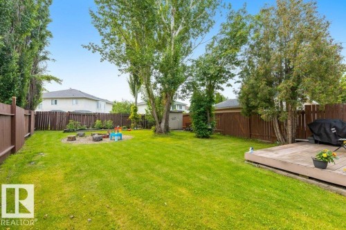 Expansive backyard featuring a manicured lawn, established trees, a wood deck, a circular gravel area, and full privacy fencing - 18609 54 Avenue, Edmonton, AB 