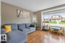 Living area with wood-finish flooring, neutral wall tones, and a large picture window providing abundant natural light - 18609 54 Avenue, Edmonton, AB 