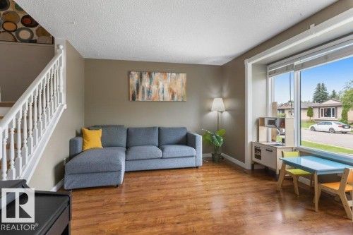 Spacious living area featuring wood-finish flooring, a prominent bay window, and a white staircase with classic balusters - 18609 54 Avenue, Edmonton, AB 