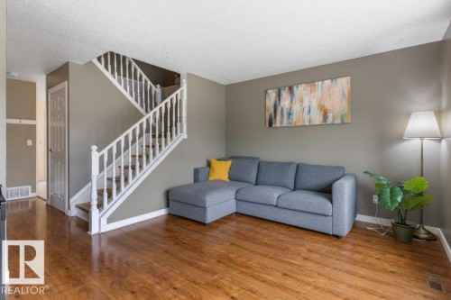 Spacious living area featuring wood-finish flooring, a white spindle staircase, and neutral wall tones - 18609 54 Avenue, Edmonton, AB 