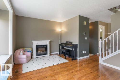 Living area featuring wood-finish flooring, a white fireplace with a dark insert, a white-painted staircase, and neutral wall tones - 18609 54 Avenue, Edmonton, AB 