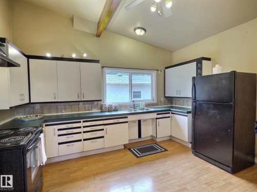 Kitchen featuring wood-finish flooring, vaulted ceilings, white cabinetry with black accents, a double basin sink, and a black range - 79 Grosvenor Boulevard, St. Albert, AB 