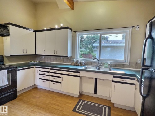 Kitchen featuring light wood-finish flooring, white cabinetry with black accents, a double basin stainless steel sink, and a tiled backsplash - 79 Grosvenor Boulevard, St. Albert, AB 