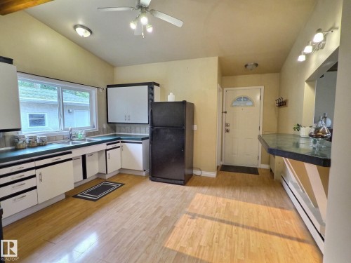 Kitchen featuring light wood-finish flooring, white cabinetry with black accents, a window over the sink, and a black refrigerator - 79 Grosvenor Boulevard, St. Albert, AB 
