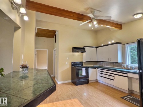 Kitchen featuring wood-finish flooring, vaulted ceilings with exposed wood beams, white cabinetry, and a green tiled countertop island - 79 Grosvenor Boulevard, St. Albert, AB 