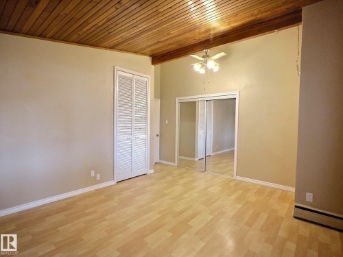 Spacious room featuring a wood-panel vaulted ceiling, wood-finish flooring, mirrored closet doors, louvered bi-fold closet doors, and an overhead ceiling fan with lighting - 79 Grosvenor Boulevard, St. Albert, AB 