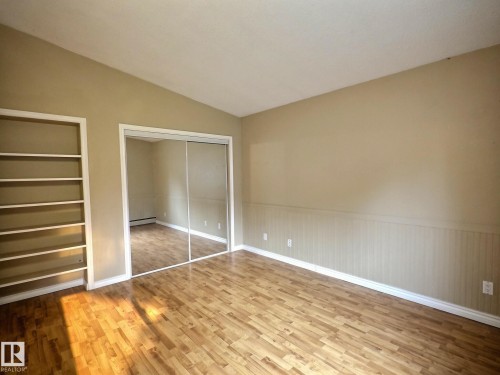 Spacious room featuring wood-finish flooring, built-in shelving, mirrored sliding closet doors, wainscoting, and a vaulted ceiling - 79 Grosvenor Boulevard, St. Albert, AB 