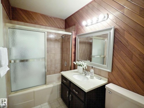 Bathroom featuring diagonal wood paneling and a bathtub with a sliding glass enclosure - 79 Grosvenor Boulevard, St. Albert, AB 